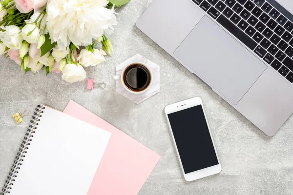 Stylish concrete stone office desk table with laptop computer, cup of coffee, flowers, female hand writing text in paper diary notepad. Top view with copy space, flat lay. Feminine workspace concept — Stock Photo, Image