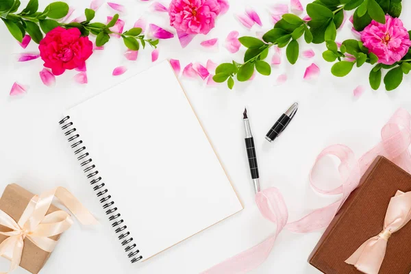 Composición elegante con flores rosadas, bloc de notas de papel en blanco, cinta, caja de regalo de la pluma sobre fondo blanco. Escritorio de oficina en casa de mujer, cama plana, vista superior . — Foto de Stock