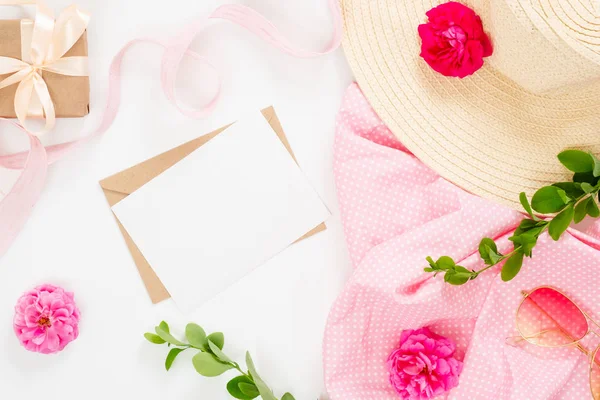 Düz yatıyordu moda ofis masa masası. Boş kağıt kartı, zanaat zarf, hasır şapka, gül çiçek tomurcukları, hediye kutusu, beyaz arka plan üzerinde dalları ile Kadın çalışma alanı. Üst görünüm kadınsı arka plan