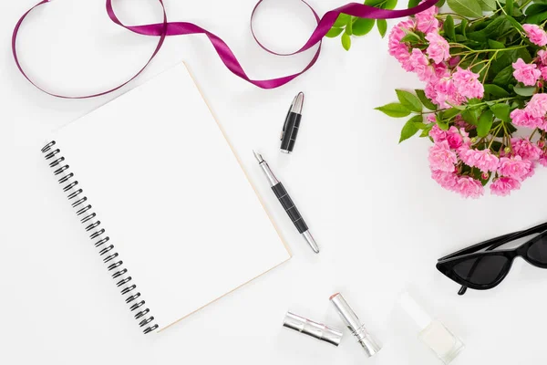 Moderno espacio de trabajo de escritorio de oficina en casa con bloc de notas de papel en blanco, accesorios femeninos, gafas, ramo de flores de color rosa sobre fondo blanco. Mesa femenina plana, vista superior . — Foto de Stock