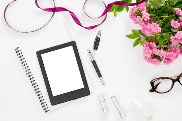 Moderne Home Office Desk werkruimte met leeg scherm Tablet e-boek, vrouwelijke accessoires, glazen, papieren notitieboekje, boeket van roze roos bloemen op witte achtergrond. Platte lay vrouwelijke tafel, bovenaanzicht. — Stockfoto