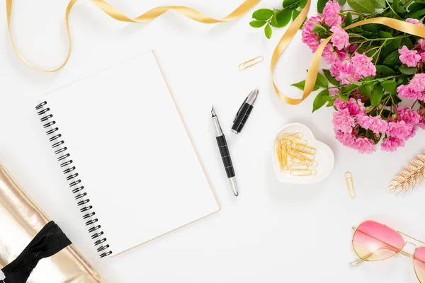 Moderno espacio de trabajo de escritorio de oficina en casa con bloc de notas de papel en blanco, accesorios femeninos, gafas, ramo de flores de color rosa sobre fondo blanco. Mesa femenina plana, vista superior . — Foto de Stock