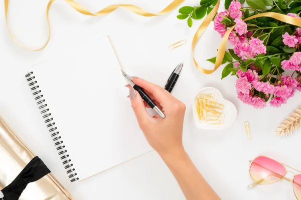 Flat Lay divat irodai íróasztal. Női munkaterület üres papír notebook és a kezét a nő kezében toll, rózsaszín rózsa virág, arany kiegészítők, napszemüveg. Felülnézet nőies háttér. — Stock Fotó
