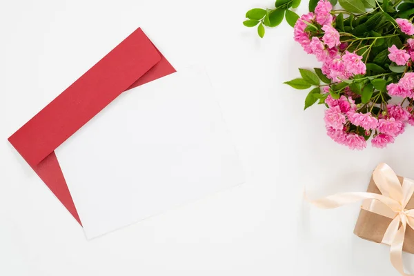 Flat lay home office desk. Women workspace with blank paper card, red paper envelope, pink rose flowers, gift box. Top view feminine background. Writing love letter concept.