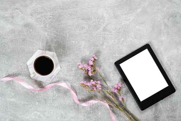 Flat lay elegantes accesorios femeninos: taza de café, cinta rosa, flores secas y lector de libros electrónicos en la superficie de hormigón. Top view beauty blogger workspace, freelancer home office desk. Héroe del blog . — Foto de Stock