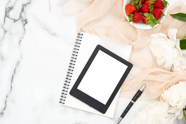 Üst görünüm e-kitap okuyucu, kağıt not defteri, şakayık çiçekler, çilek, mermer arka plan üzerinde pastel renkli eşarp. Kadınsı aksesuarları ile minimal düz yatıyordu stil kompozisyon. Moda veya güzellik blog afiş.