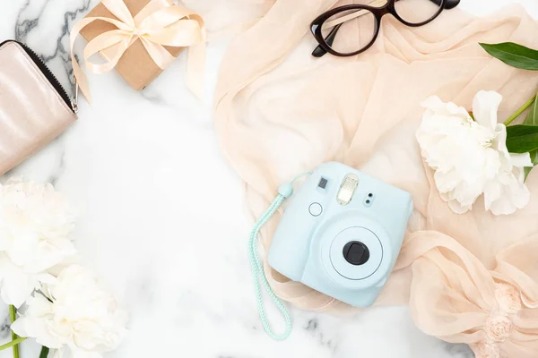 Fashion blog banner mockup with trendy feminine accessories. Flat lay instant film camera, glasses, purse, pastel pink woman scarf, white peony flowers on marble background. Beauty and fashion concept