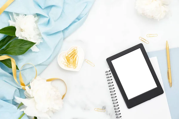 Flat lay feminine home office workspace with peony flowers, paper notepad, e-book reader and golden decorations on marble background. Top view women desk, fashion blog banner template. — Stock Photo, Image