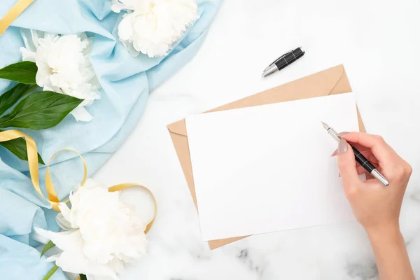 Top view mujer mano escritura boda invitación tarjeta o carta de amor. Composición plana mínima con flores de peonía, artículos de papelería y accesorios femeninos. Escribir el concepto de carta —  Fotos de Stock