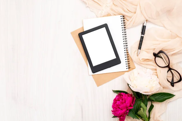 Blogger de moda escritorio de oficina en casa con artículos de mujer: lector de libros electrónicos moderno, bloc de notas de papel, bufanda beige, peonías flores, gafas. Vista superior, composición de estilo laico plano mínimo tierno . —  Fotos de Stock