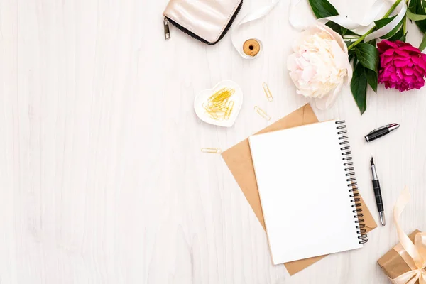 Piso en casa escritorio de la oficina. Espacio de trabajo femenino con cuaderno de papel, ramo de flores de pión, accesorios dorados, bolso sobre fondo de madera. Vista superior de fondo femenino. Plantilla de banner blog de moda . —  Fotos de Stock