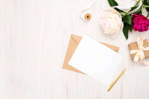 Colocar flores de peonías planas, sobre artesanal, tarjeta de papel en blanco, caja de regalo, pluma, cinta sobre fondo de madera. Espacio de trabajo femenino de vista superior, maqueta de tarjeta de invitación de boda, composición mínima tierna . — Foto de Stock