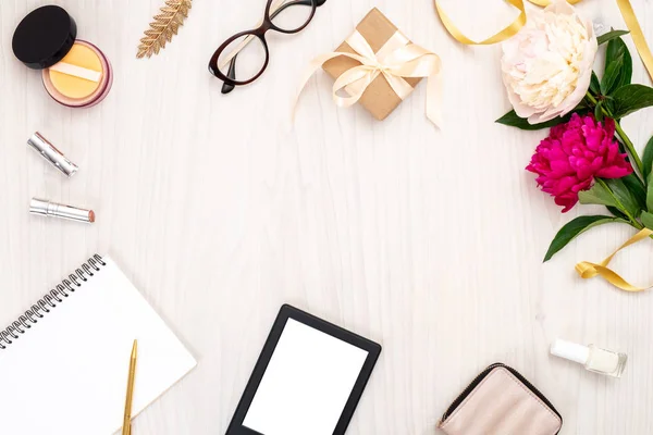 Övre vy ram gjord av kvinnor objekt: e-bok, papper anteckningsblock, handväska, Glasögon, kosmetiska, pion blommor. Minimal Flat Lay stil komposition med feminina tillbehör, Home Office Desk Concept. Kopiera utrymme. — Stockfoto