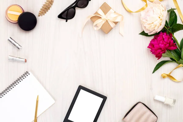 Övre vy ram gjord av kvinnor objekt: e-bok, papper anteckningsblock, handväska, Glasögon, kosmetiska, pion blommor. Minimal Flat Lay stil komposition med feminina tillbehör, Home Office Desk Concept. Kopiera utrymme. — Stockfoto