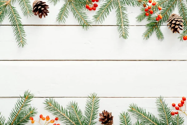 Noel çerçeve köknar ağacı dalları, kırmızı çilek, rustik ahşap beyaz arka plan üzerinde çam kozalağa yapılmış. Noel, Yeni Yıl, kış tatilleri kavramı. Düz döşeme, üst görünüm, kopyalama alanı