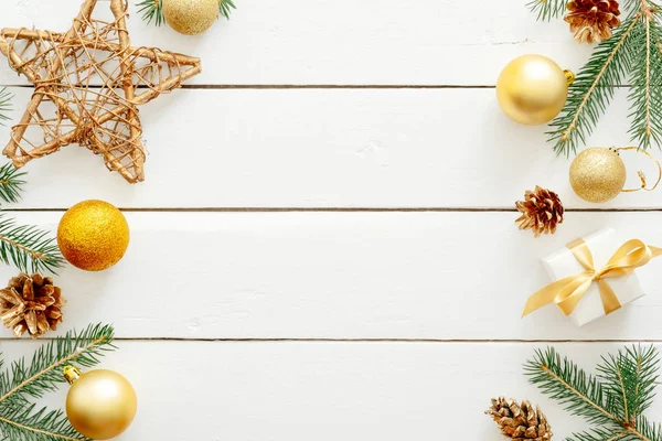 クリスマスの作曲。金色の装飾、装飾品、星、贈り物、モミの木の枝、素朴な木製の白い机の上の松ぼっくりで作られたクリスマスフレーム。クリスマス、新年、冬のコンセプト。フラットレイ. — ストック写真
