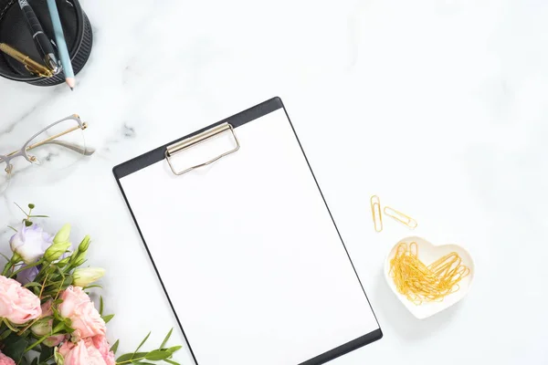 Espacio de trabajo moderno de escritorio de oficina en casa con portapapeles en blanco, ramo de flores de rosas, gafas, papelería dorada sobre fondo de mármol blanco. Pisos, vista superior . — Foto de Stock