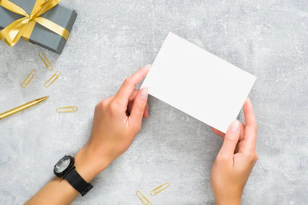 Hediye kutusu ile beton taş masada boş kağıt kart mockup tutan eller. ve altın klipler. Düz döşeme, üst görünüm, kopyalama alanı.