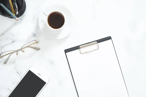 Flatlay av hem kontor skrivbord arbetsyta med papper Urklipp, kaffekopp, Glasögon, smartphone, brevpapper på vit marmor sten bakgrund. Topputsikt feminin arbetsplats, skönhet teknikkoncept. — Stockfoto