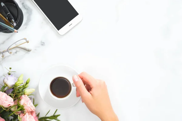 Flat Lay, topputsikt kontorsbord. Feminint skrivbord arbetsyta ram med kaffekopp, blommig bukett, Glasögon, smartphone och brevpapper på vit marmor bakgrund. — Stockfoto