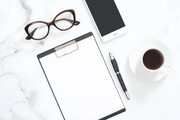 Modern hem kontor skrivbord arbetsyta med tomma papper Urklipp, Glasögon, brevpapper, smartphone på vit marmor bakgrund. Flatlay, topputsikt. — Stockfoto