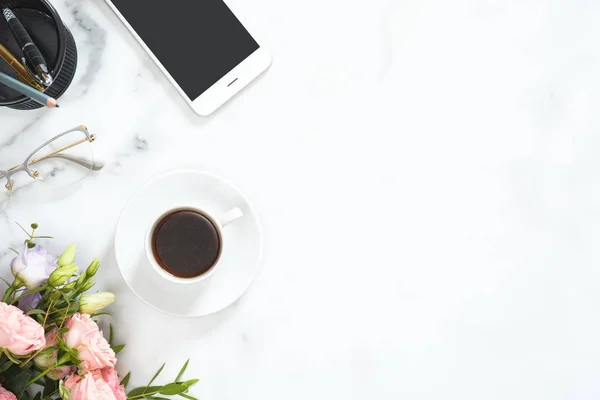 Flat Lay, topputsikt kontorsbord. Feminint skrivbord arbetsyta ram med kaffekopp, blommig bukett, Glasögon, smartphone och brevpapper på vit marmor bakgrund. — Stockfoto