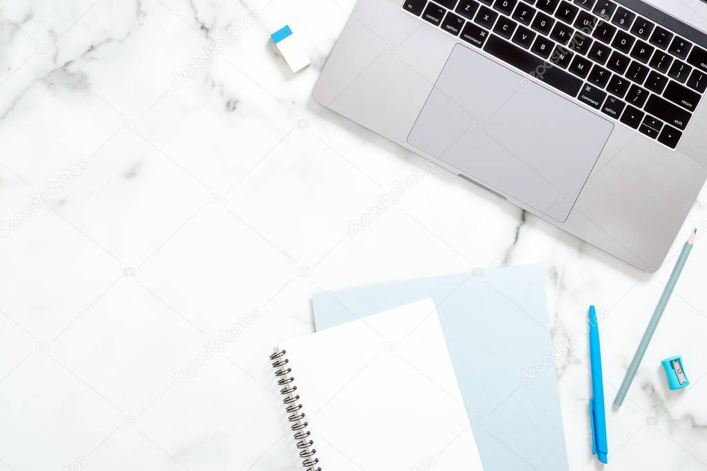 Marble office desk table with laptop computer, paper notepad, blue stationery. Minimal flat lay style composition, top view, overhead. Business woman workspace concept.