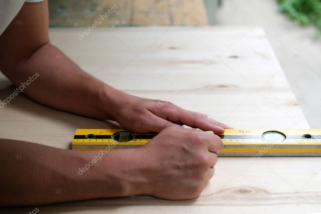 Carpenter marking straight line on plywood sheet using spirit level in carpentry workshop. Measuring, drawing line, DIY concept.