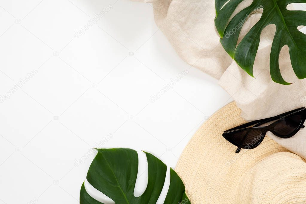 Summer vacation concept with tropical monstera leaves, straw hat and feminine sunglasses on white background. Minimal flat lay style composition with copy space. Top view, overhead.