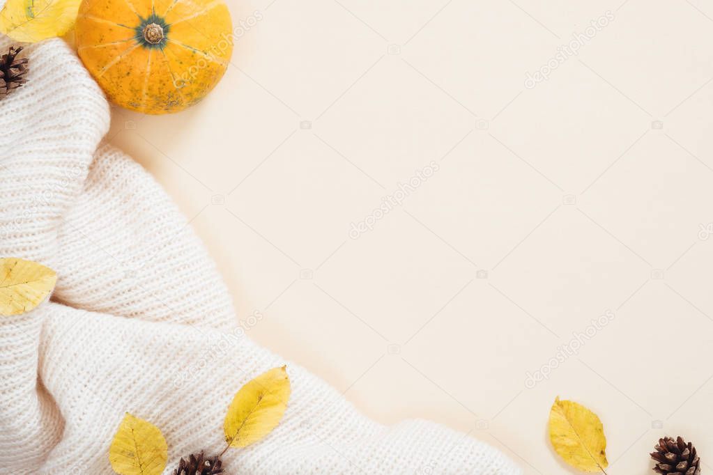 Flatlay autumn composition. Orange pumpkin, white knitted scarf, dry autumn leaves, cones on pastel beige background. Autumn minimal concept. Flat lay, top view.