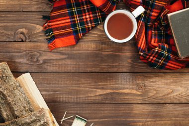 Kırmızı eşarp, çay fincan, yakacak odun, ahşap masa üzerinde kitap ile Flatlay kompozisyon. Hygge tarzı, rahat sonbahar veya kış tatili konsepti. Düz döşeme, üst görünüm, genel merkez.