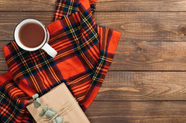 Kırmızı eşarp, çay fincan, ahşap masa üzerinde hediye kutusu ile Flatlay kompozisyon. Hygge tarzı, rahat sonbahar veya kış tatili konsepti. Düz döşeme, üst görünüm, genel merkez.