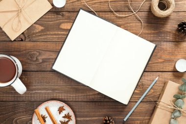 Boş kitap, çay fincan, zanaat zarf, kalem, hediye kutusu, tarçın çubukları, ahşap arka plan üzerinde mevcut ile Flatlay kompozisyon. Rahat sonbahar veya kış tatili konsepti. Düz döşeme, üst görünüm, kopyalama alanı