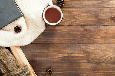 Beyaz örme eşarp, çay fincan, kitap, ahşap masa üzerinde yakacak ağacı ile Flatlay kompozisyon. Hygge tarzı, rahat sonbahar veya kış tatili konsepti. Düz döşeme, üst görünüm, genel merkez.