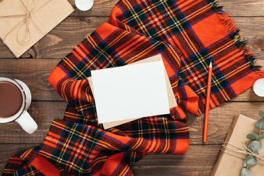 Kırmızı örme eşarp, çay fincan, zanaat zarf, kalem, ahşap arka plan üzerinde hediye kutusu ile Sonbahar flatlay kompozisyon. Rahat sonbahar veya kış tatili konsepti. Düz döşeme, üst görünüm, kopyalama alanı