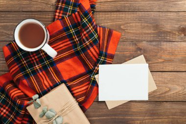Sonbahar kompozisyonu. Çerçeve kırmızı örme eşarp, mektup, boş kağıt kart, çay bardağı, ahşap arka plan üzerinde hediye kutusu yapılmış. Rahat sonbahar veya kış tatili konsepti. Düz döşeme, üst görünüm, kopyalama alanı