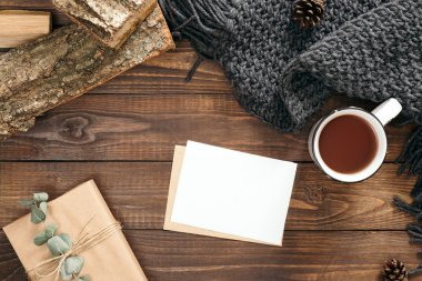 Mektup, boş kağıt kart, çay fincan, moda kadınsı örme eşarp, hediye kutusu, ahşap arka plan üzerinde yakacak odun ile Nordic hygge tarzı flatlay kompozisyon. Düz yatıyordu, üstten bak, tepede. Rahat ev masası