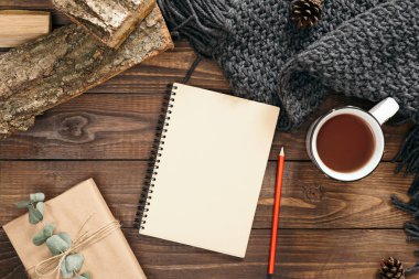 Sonbahar kompozisyonu. Boş kağıt not defteri, çay fincanı, kadın moda kazak, hediye kutusu, ahşap arka plan üzerinde yakacak odun. Düz döşeme, üst görünüm, kopyalama alanı. İskandinav hygge kavramı.