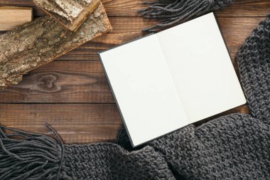 Boş sayfa, gri örme eşarp, ahşap arka plan üzerinde yakacak odun ile Flatlay kitap. Düz yatıyordu, üstten bak, tepede. Rahat sonbahar ev masası masası