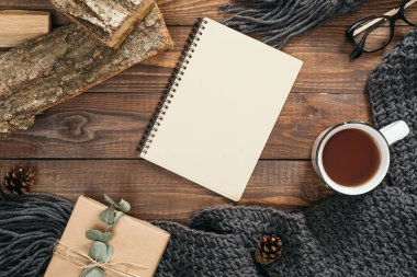 Moda kadın örgü eşarp, boş kağıt defter, çay bardağı, hediye kutusu, ahşap arka plan üzerinde yakacak odun ile Flatlay hygge tarzı kompozisyon. Düz yatıyordu, üstten bak, tepede. Rahat sonbahar ev masası