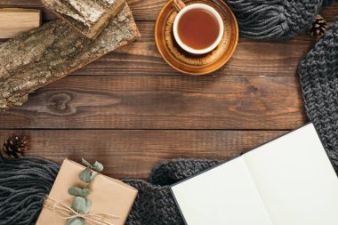Çay fincan, moda örme eşarp, hediye kutusu, ahşap arka plan üzerinde yakacak odun ile Hygge tarzı flatlay çerçeve. Düz yatıyordu, üstten bak, tepede. Rahat sonbahar ev masası konsepti