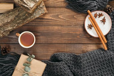 Moda kadın örgü eşarp ile Flatlay hygge tarzı kompozisyon, çay bardağı, hediye kutusu, yakacak odun, ahşap arka plan üzerinde tarçın sopalarla. Düz yatıyordu, üstten bak, tepede. Rahat sonbahar ev masası konsepti