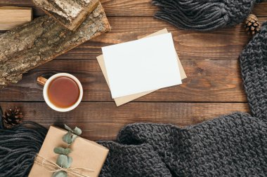 Moda kadın örgü eşarp, mektup, boş kağıt kart, çay bardağı, mevcut, ahşap arka plan üzerinde yakacak odun ile Flatlay hygge tarzı kompozisyon. Düz yatıyordu, üstten bak, tepede. Rahat sonbahar ev masası