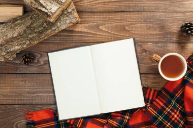 Boş sayfaları, çay fincan, rahat örme eşarp, ahşap arka plan üzerinde yakacak odun ile Flatlaly kitap. Sonbahar natürmortu, klasik masa masası. Düz yatıyordu, üst görünüm, havai, İskandinav hygge tarzı kavramı