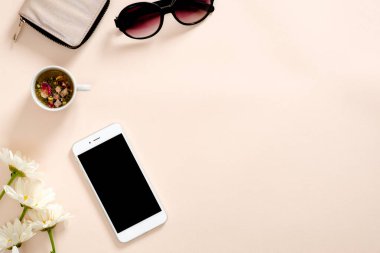 Kadınsı aksesuarları ile Flatlay kompozisyon, çay bardağı, akıllı telefon boş ekran mockup, güneş gözlüğü, pastel pembe arka plan papatya çiçekler. Kadınsı ev ofis masası konsepti. Düz döşeme, üst görünüm