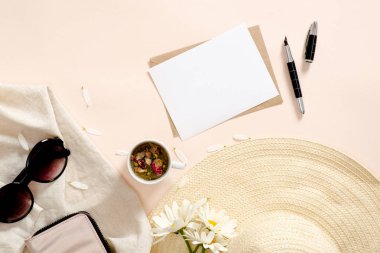 Yaz moda aksesuarları, hasır şapka, giysi, çay bardağı, boş kağıt kart mockup, pastel pembe arka plan papatya çiçekler ile Flatlay kompozisyon. Düz yatıyordu, üstten bak, tepede. Moda blogger masası.