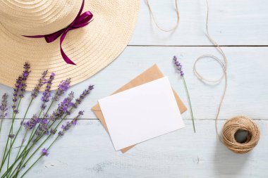 Vintage zarf, boş kağıt kart mockup, lavanta çiçekleri, hasır şapka ve rustik mavi ahşap arka plan üzerinde ip. Romantik kompozisyon, aşk mektubu kavramı. Düz döşeme, üst görünüm, genel merkez.