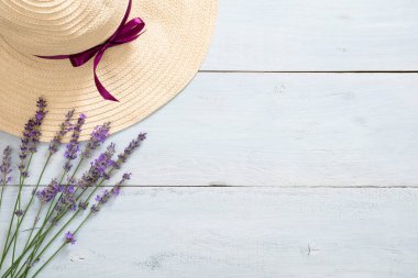 Rustik mavi ahşap arka plan üzerinde hasır şapka ve lavanta çiçekleri ile Flatlay kadınsı masa. Düz döşeme, üst görünüm, kopyalama alanı. Yaz moda konsepti.