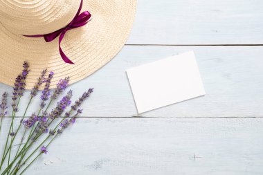 Hasır şapka, lavanta çiçekleri ve rustik mavi ahşap arka plan üzerinde boş kağıt kart mockup ile Flatlay kadınsı masa. Düz yatıyordu, üstten bak, tepede. Yaz moda konsepti.