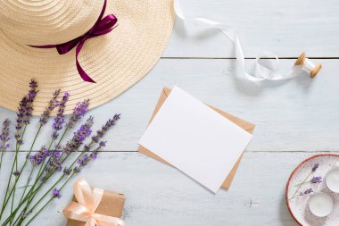 Hasır şapka, lavanta çiçekleri, kağıt kart maket, zanaat zarf, kurdele, hediye kutusu, mumlar ile Flatlay kompozisyon. Romantik aksesuarları ile kadınsı masa masa. Düz döşeme, üst görünüm, genel merkez